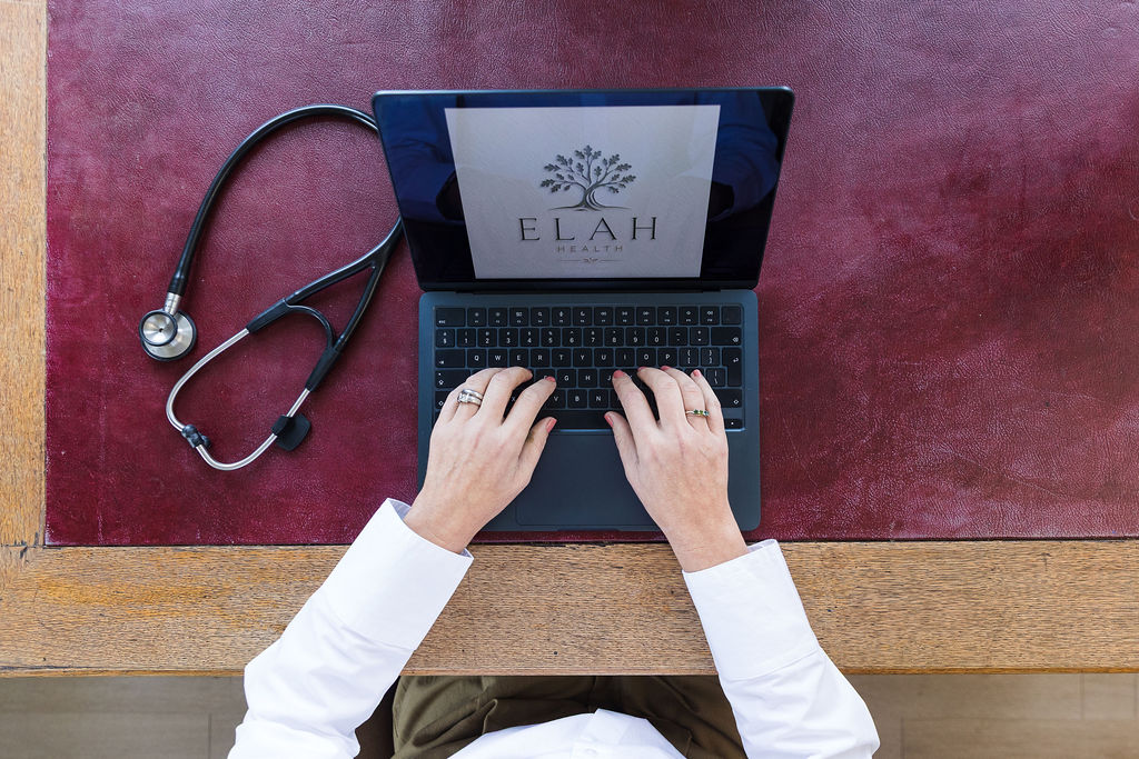 Hands typing on a laptop showing the Elah Health logo, beside a stethoscope